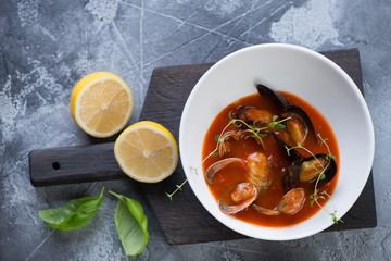 Tomato soup with seafood in a white bowl on a black wooden serving board, above view on a grey stone background