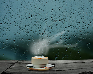 Steaming coffee cup on a rainy day window background