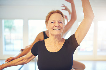 Mature smiling woman standing with hand up in ballet class
