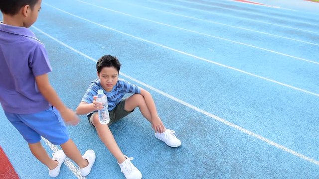young Asian Thai boy drinking water from bottle during resting on the blue track after running