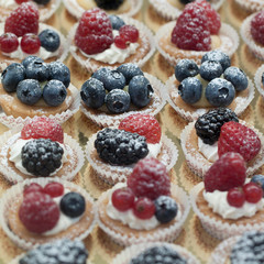 A variety of cakes with berries stacked in rows in a shop window in a cafe