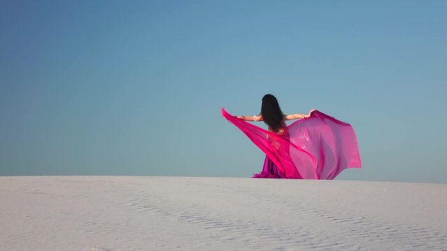 Dancer in the sandy desert in the hands of a pink pink veil. Slow motion