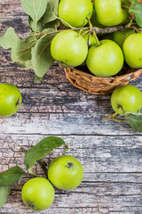  Fresh green apples with leaves in a wicker basket on a old wooden table. A new crop. The concept of a healthy diet. Top view.