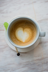 A cup of coffee with heart pattern in a white cup on white marble background and green sugar stick, latte coffee