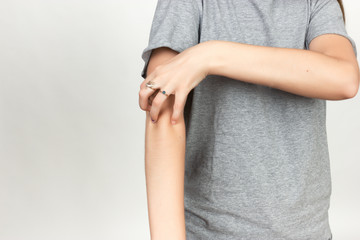 Girl in grey shirt scratching her arm. Scabies. Scratch the hand
