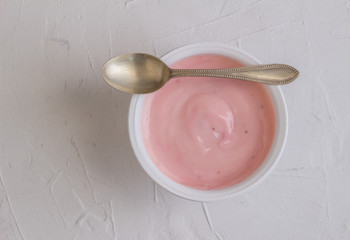 Healthy strawberry fruit flavored yogurt with natural coloring in plastic cup isolated on white rustic background with little silver spoon - top view shot in studio