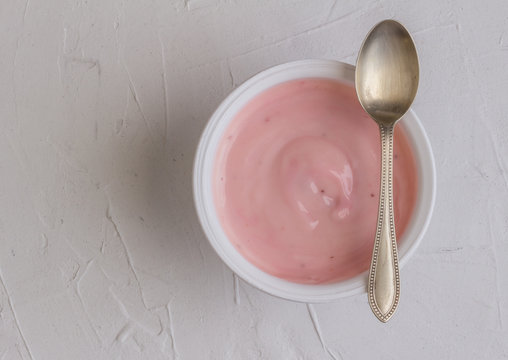 Healthy strawberry fruit flavored yogurt with natural coloring in plastic cup isolated on white background with little silver spoon   - top view shot in studio