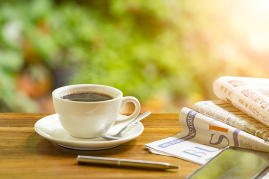 coffee cup with newspaper on a wooden table. Image is overexposed from the right bottom corner.