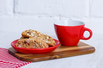 House biscuit of cantuccini or cantucci, the Italian cookies, on a saucer of red color with a cup of coffee on a white background