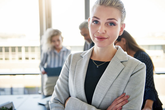 Confident young businesswoman with coworkers talking in the background