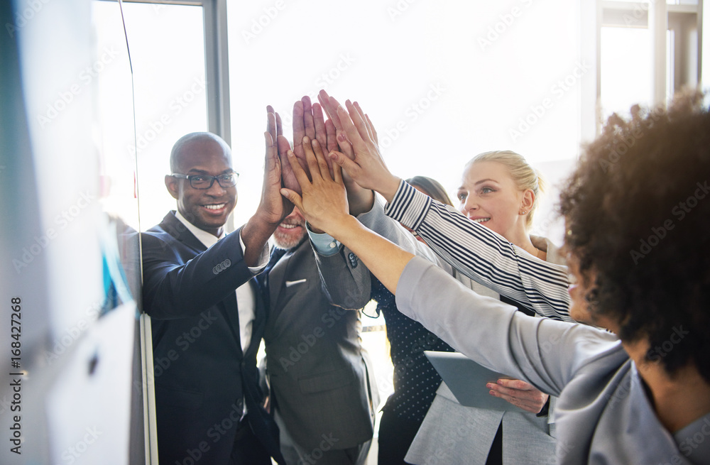 Wall mural smilling colleagues high fiving each other in a modern office