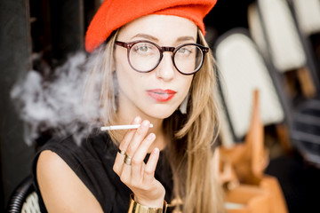 Portrait of a young stylish woman in red beret and eyeglasses smoking a cigarette