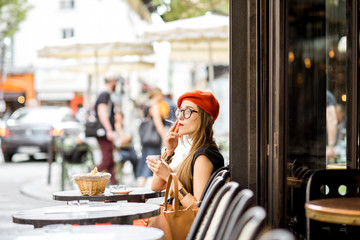 Young stylish woman in red beret smoking a cigarette sitting outdoors at the french cafe