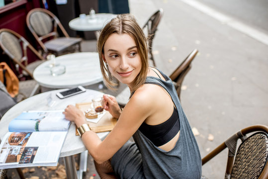 Portrait of a young and pretty woman in gray dress sitting outdoors at the french cafe