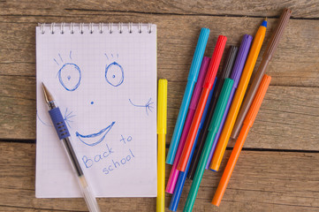 Open white notepad with drawing and inscription BACK TO SCHOOL with colorful felt-tip pens and ball pens on the wooden table