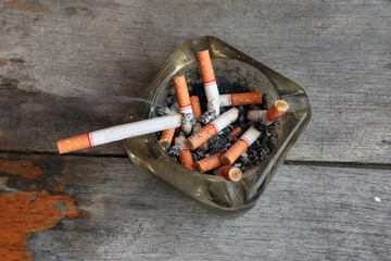 Cigarette put on the Full ashtray of cigarettes, on the wooden table. ashtray is a receptacle for tobacco ash and cigarette butts.