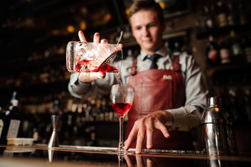 close up bartender pouring bright red alcohol cocktail into fancy glass