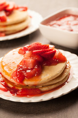 
Freshly made white flour pancakes stacked on white plates topped with red strawberry syrup macro shot
