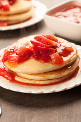 
Freshly made white flour pancakes stacked on white plates topped with red strawberry syrup close up shot
