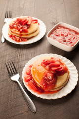 
Freshly made white flour pancakes stacked on white plates topped with red strawberry syrup vertical shot
