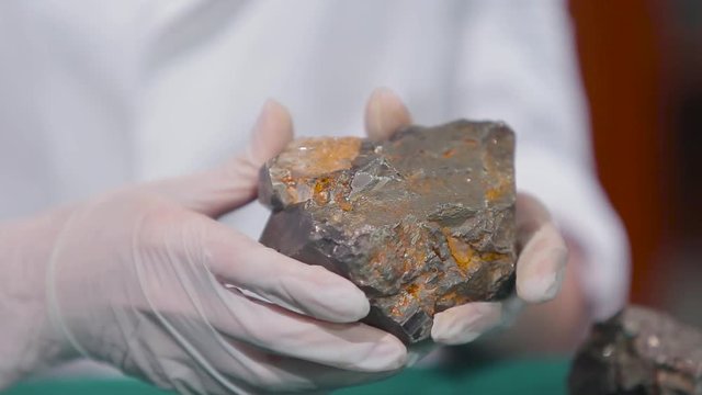 Female hands in white gloves holding stone mineral. Stone macro, gray rough stone. Fluorite mineral stone, fluorite mineral stone. Scientist studying the stone material close up