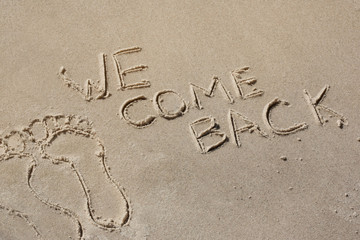 We come back - written by hand in sand on a sea beach, with a soft wave. End of rest, holiday.