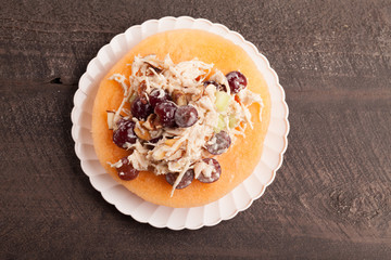 
Cantaloupe ring filled with chicken grape cantaloupe salad on a white plate and dark wooden background above view
