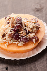 
Cantaloupe ring filled with chicken grape cantaloupe salad on a white plate and dark wooden background close up shot

