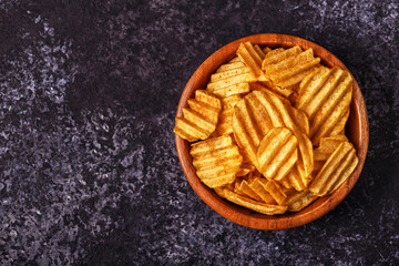 Crispy potato chips in a bowl on stone background.
