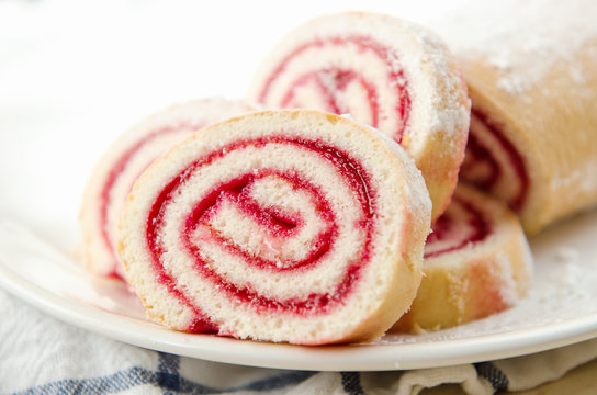 Fresh sweet roll with strawberry jam and powdered sugar on a plate and white towel