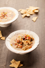 
White chicken chili with red peppers, chicken, and beans in white bowl with corn tortilla chips slightly above shot
