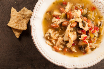 
White chicken chili with red peppers, chicken, and beans in white bowl with corn tortilla chips close up shot
