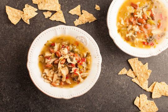
White chicken chili with red peppers, chicken, and beans in white bowl with corn tortilla chips horizontal shot
