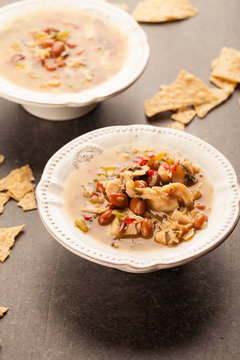 
White chicken chili with red peppers, chicken, and beans in white bowl with corn tortilla chips vertical shot
