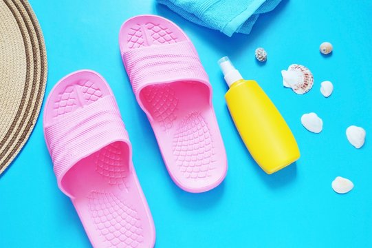 Flat lay beach background/ Pink slippers, a yellow bottle with sunscreen, seashells, a hat and a towel