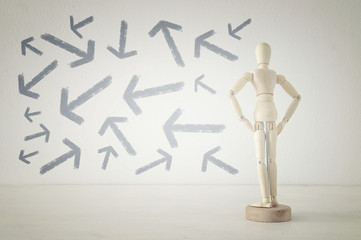 wooden person standing with his back in front of textured background full of arrows pointing in different directions