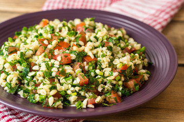 Tabbouleh salad with bulgur, tomatoes, parsley, green onion and mint in plate on wooden table.