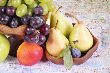 Light and dark grapes in a wooden bowl with an apple pear plum and figs on an abstract background.Fruit still life