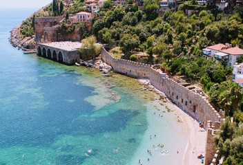 Vacationers bathe and sunbathe against the background of the ancient fortress wall (Alanya, Turkey).