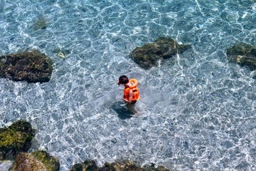 A boy in an orange lifejacket stands in crystal clear water (Alanya, Turkey).