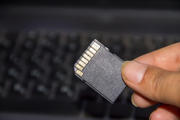 Hand holding SD card on laptop background