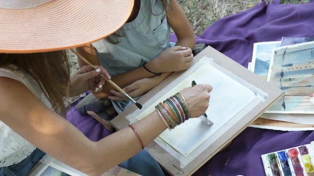 A lesson in drawing of watercolor paints for young girl on the nature at park