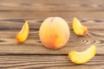 One whole fresh ripe peach and three slices of peach on old rustic wooden planks