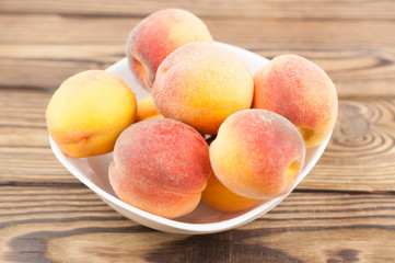 Lot of fresh whole ripe peaches in white ceramic bowl on rustic old wooden planks
