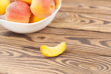 Lot of fresh whole ripe peaches in white ceramic bowl and one slice of peach separately on rustic old wooden planks