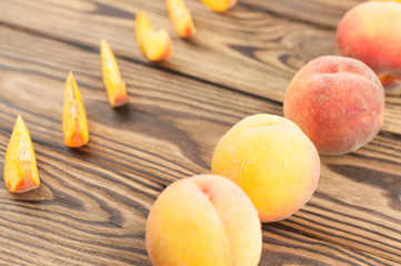 Row of slices of fresh ripe peach and whole peaches scattered on rustic old wooden planks