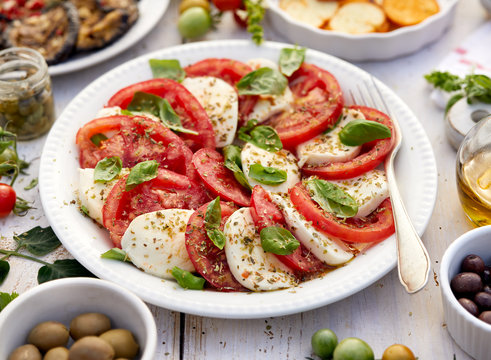 Caprese salad made of sliced fresh tomatoes, mozzarella cheese and basil  served on a white plate on a wooden table.Traditional Italian food
