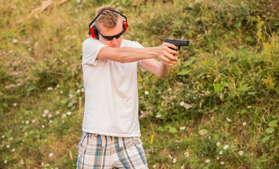 Young and strong caucasian blond guy firing bullets at the enemy target in the wilderness. Aiming to shoot with his gun  pistol showing professional police skills in the nature.