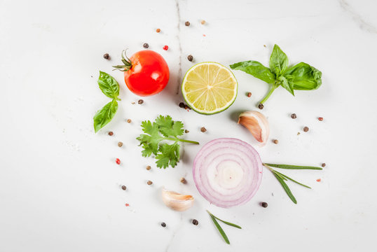 Food cooking background, white marble kitchen table. Spices and herbs for cooking dinner - coriander, parsley, basil, rosemary, lime, tomato, salt, pepper, garlic, onion, tomato. Copy space top view