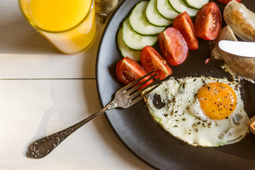 Fried eggs with tomatoes and cucumbers on a rustic wooden background